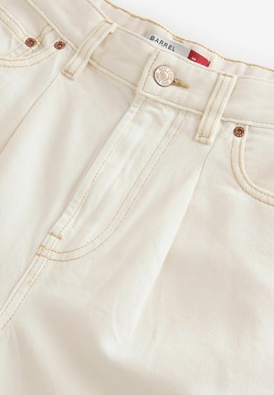 Krémové kalhoty s jemnou texturou, vybavené zipem, bronzovým kováním a kontrastním stehem podél švů a kapes.
