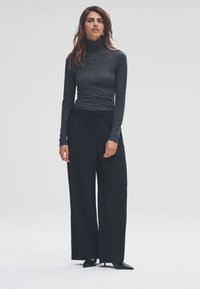 Langærmet, mørkegrå rullekravebluse kombineret med sorte bukser med vide ben. Bukserne har elastisk linning og tekstureret stof. Sorte spidse sko.