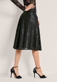 Zwarte kanten midi-rok met een vloeiende design en subtiele glans, gecombineerd met zwarte hoge hakken met versieringen op de hak.