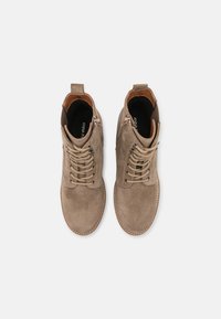 Par de botas de ante beige hasta el tobillo con cordones y cremalleras laterales, vistas desde arriba sobre un fondo gris claro.
