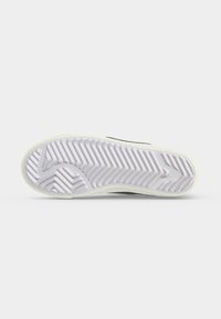 Shoe sole with white zigzag tread pattern and arrow shapes on a plain light gray background.