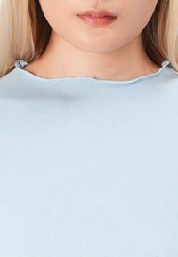 Nebesko plava, rebrasta pamučna majica s okruglim izrezom i lagano pohabanim rubom na ovratniku. Minimalistički dizajn, bez uzoraka ili metalnih dijelova.