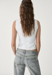 Top sans manches blanc associé à un jean en denim gris taille haute. Le jean a une texture décolorée et des poches arrière visibles.