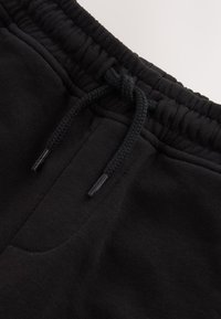 Pantalon de survêtement noir en gros plan montrant une ceinture élastique avec un cordon noué et une couture de poche visible.