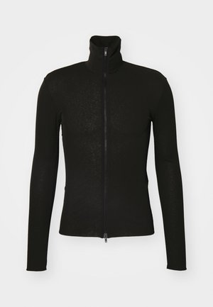 Schwarze Zip-Jacke aus einem strukturierten Stoff, mit langen Ärmeln und hohem Kragen. Der Front-Reißverschluss reicht vom Kragen bis zum Saum.