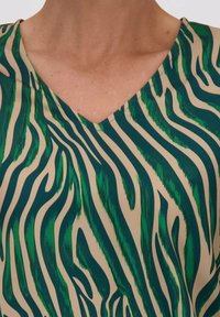 Korte mouwen V-hals top in een beige stof met groene en donkergroene zebrapatroon, met een gladde textuur en reguliere pasvorm.