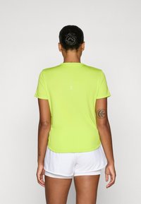 Koszulka sportowa krótki rękaw, jasno limonkowa z okrągłym dekoltem. Posiada białe paski akcentujące z tyłu oraz gładką, rozciągliwą fakturę.