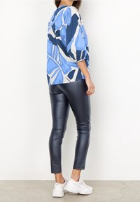 Top bluetto con motivo, con maniche a palloncino, abbinato a leggings scuri lucidi. L'insieme presenta una vestibilità rilassata e un design moderno.