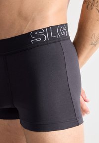 Boxer shorts en coton noir avec une taille élastique comportant le nom de la marque brodé en blanc, design ajusté et texture lisse.