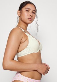 Sutiã amarelo claro com padrão floral texturizado, alças ajustáveis e fecho de gancho, combinado com um fundo de bikini floral cor-de-rosa.