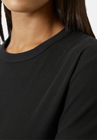 Close-up of a person wearing a black ribbed crew neck top, showing neckline, shoulder, and long dark hair.