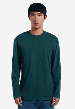 Groene lange mouwen shirt van zachte stof met een ronde hals en een subtiel logo op de borst. Gecombineerd met denim jeans.