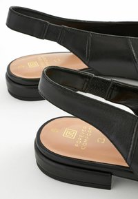 Fekete bőr pántos szandál sima textúrával, párnázott talpbetéttel és lapos talppal. Rugalmas pánt a megfelelő illeszkedés érdekében, és logó részlet a talpbetéten.