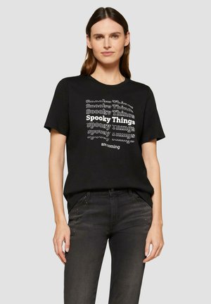 T-shirt noir avec un design en texte blanc répété : "Choses Effrayantes", avec des styles de police variés. Manches courtes, col rond, coupe décontractée.