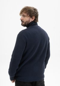 Donkerblauwe gebreide trui met een hoge kraag, gestructureerd ribpatroon en lange mouwen, gezien vanuit de achterkant, tegen een witte achtergrond.