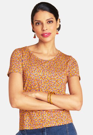 Short-sleeve top in orange with a colorful circular pattern, round neckline, and soft texture. Paired with blue jeans and gold accessories.