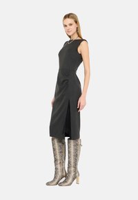 Abito nero senza maniche con spacchi al ginocchio, caratterizzato da un corpetto aderente. Abbinato a stivali argento al ginocchio in stampa pitone e dettagli metallici.