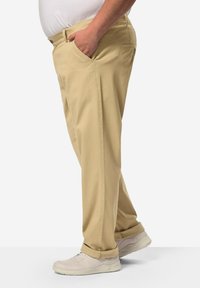 Chino khaki con tasche laterali, design a gamba dritta, tessuto in misto cotone e dettagli con risvolto, abbinati a sneakers di colore chiaro.