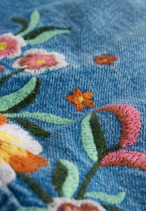 Broderad denim med en blå bakgrund har olika blommor i rosa, orange och vitt, tillsammans med gröna blad och detaljerad sömnad.