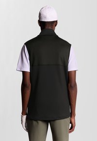 Gilet de golf noir sans manches en tissu lisse, avec un col montant et une chemise blanche à manches courtes en contraste en dessous.