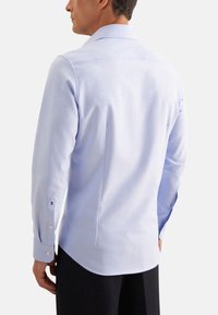 Camicia azzurra chiara con colletto, maniche lunghe, polsini a bottone, tessuto morbido e orlo curvo. La vista posteriore mostra le cuciture delle spalle e una vestibilità su misura.