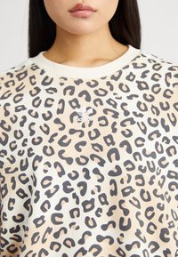 Sweatshirt med leopardmönster i lättviktig tyg; har rund halsringning och en broderad vit adidas-logotyp framtill.