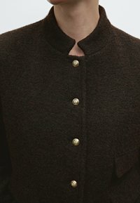 Dark brown wool jacket with a high collar, featuring five gold buttons and a textured surface. Includes a side pocket.