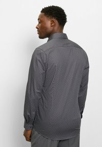 Long-sleeve shirt in dark gray fabric with circular patterns in light gray and cream. Features a classic collar and rounded hemline.