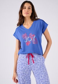 Camiseta azul de cuello en V con mangas cortas, que presenta un gráfico de "JOY" en hojas rojas y blancas. Combinada con pantalones azules con estampado y cordón rojo.