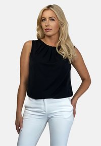 Czarna bezrękawnikowa bluzka z plisowanym dekoltem, w połączeniu z białymi dopasowanymi spodniami. Gładki materiał o minimalistycznym wzornictwie.