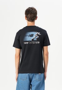 Black cotton t-shirt featuring a silver graphic of a running figure and the "New Balance" logo on the back, short sleeves, relaxed fit.