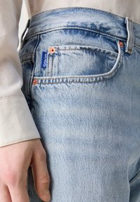 Lichtblauwe spijkerbroek van denim met een vervaagde textuur, voorzien van koperkleurige hardware en een blauwe "HUGO"-tag op de achterzak.