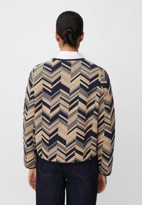 Giacca trapuntata in blu navy e beige, con un motivo a zigzag. Presenta un colletto rotondo e maniche lunghe, con una vestibilità comoda e tessuto testurizzato.