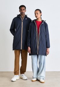 Vestes légères de marine avec des fermetures éclair contrastantes jaunes et rouges, dotées d'une capuche et de poignets réglables, portées sur des tenues en tricot colorées et en denim.