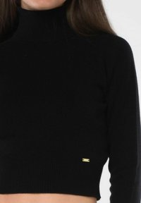 Maglione nero a collo alto cropped realizzato in tessuto a coste, con un logo in accentatura dorata all'orlo. Texture liscia, design aderente.