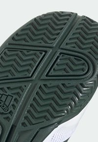 Semelle de sneaker en caoutchouc vert avec un motif de bande de roulement en zigzag. Présente le logo Adidas. La partie supérieure blanche est partiellement visible, avec un design texturé.