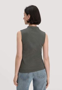 Ärmelloses Top mit hohem Kragen aus dunkelgrünem Rippstoff. Kombiniert mit hellblauen Jeans, betont die Rückansicht die Textur und Passform.