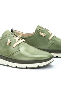 Gröna läderskor med rundad design, beige snören, perforerade detaljer och en tjock vit sula. Har en kontrasterande svart hälflik.