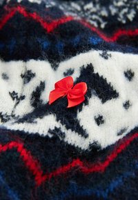 Red and navy patterned knit fabric featuring a white background with black shapes, complemented by a small red satin bow detail.