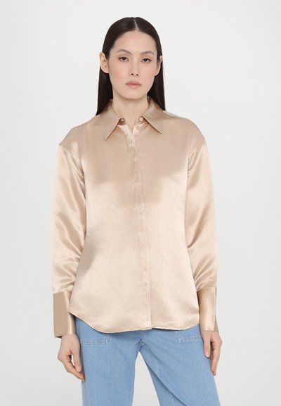 Satin beige shirt with a button-up front, pointed collar, and long sleeves. Features a smooth texture and rounded hem. Styled with light blue jeans.