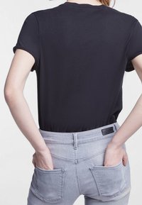 Černý body s krátkým rukávem zvýrazňuje záda, v kombinaci s vysokým pasem světle šedé džíny, které mají hladký materiál a dvě zadní kapsy.