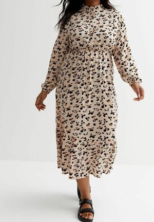Frau trägt ein beiges, langärmeliges Midikleid mit schwarzem und orangefarbenem Leopardenmuster und schwarze Sandalen mit offenen Zehen und geht vorwärts.