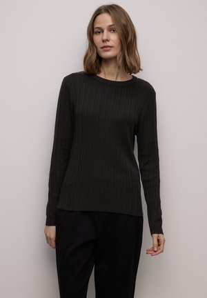 Maglia nera a maniche lunghe con costine e scollo rotondo, caratterizzata da una texture morbida. Abbinata a pantaloni scuri, su sfondo chiaro.