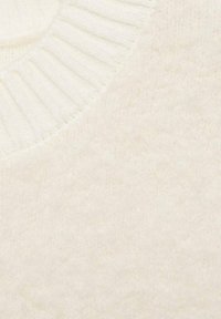 Tissu texturé couleur crème avec un col côtelé. La surface semble douce et duveteuse, contribuant à une esthétique chaleureuse.