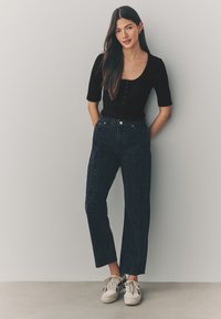 Top nero a coste con maniche corte e scollo rotondo, abbinato a jeans scuri a vita alta con motivo e sneakers di colore chiaro.