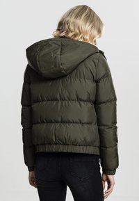 Doudoune vert olive avec capuche, présentant une couture horizontale, des poignets côtelés et une taille cintrée pour la chaleur et le confort.