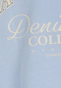 Sudadera de algodón azul claro con texto blanco que dice "Denim College" y "Established". Textura suave con un diseño informal.
