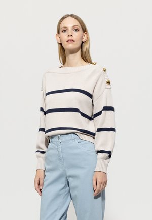 Light beige striped sweater featuring navy blue stripes, ribbed cuffs, and golden button accents on the left shoulder. Paired with light blue pants.