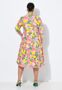 Abito floreale con sfondo rosa, limoni gialli e foglie verdi. Presenta maniche a tre quarti e un design a gonna a strati.