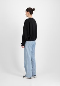 Felpa nera oversize con spalle cadenti, abbinata a jeans azzurri a vita alta. Il modello si trova davanti a uno sfondo neutro.